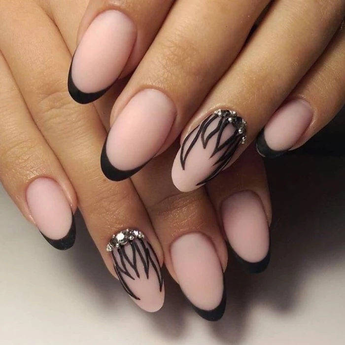 rhinestones and black, hand-drawn leaf-like patterns, decorating the ring finger nails, of two hands with nude manicure, featuring black tips