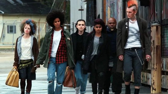 tall man with red mohawk hair, dressed in punk clothing, surrounded by young people, dressed in 80s costumes, jeans and plaid shirts