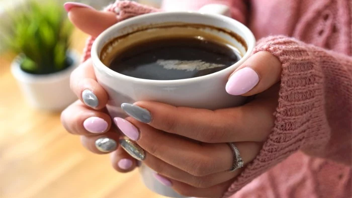full coffee mug, held by two hands, with almond shaped nails, painted in pastel pink, and creamy grey