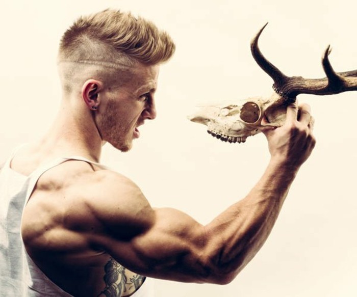 blonde man with an undercut, and a faux hawk, short haircuts for men, holding a deer skull, with one muscular arm