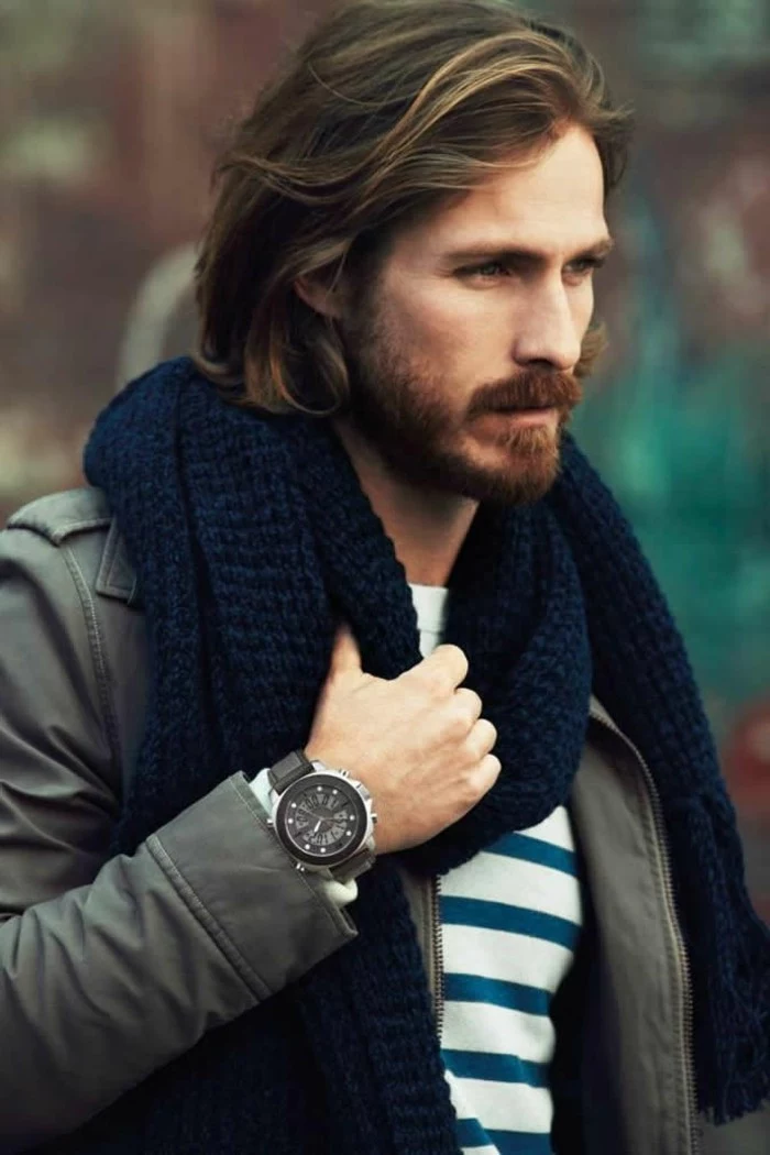 modern haircuts for men, medium length brunette hair, wavy with natural-looking highlights, worn messily slicked back, by a bearded man with a mustache