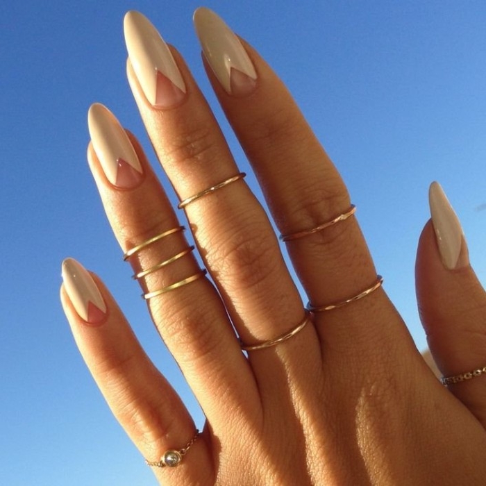 many thin gold rings, on a hand with long fingers, ending in pointy oval nails, nude nail designs, featuring small bare triangles