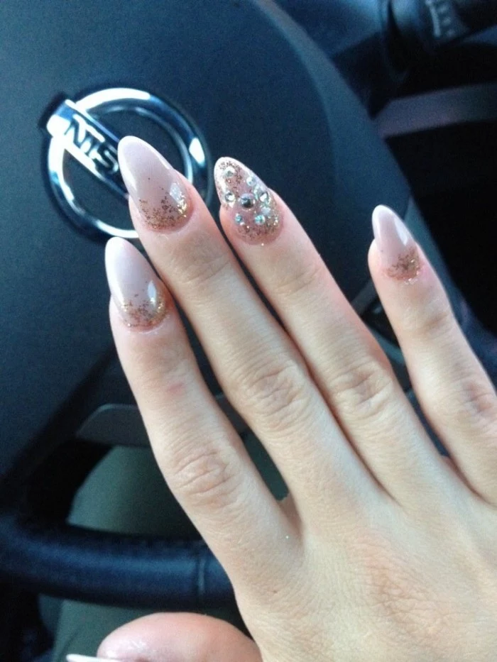 pointy nails, painted in pale pink, and decorated with glitter and rhinestones, on a hand, suspended over a steering wheel