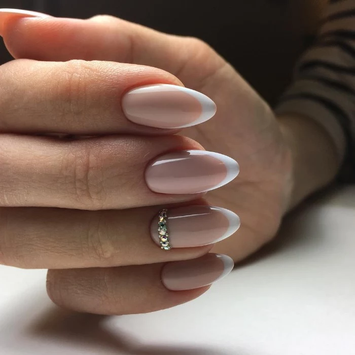 almond shaped nails, in pale nude pink, with white tips, the ring finger nail is decorated with diamante decal stones