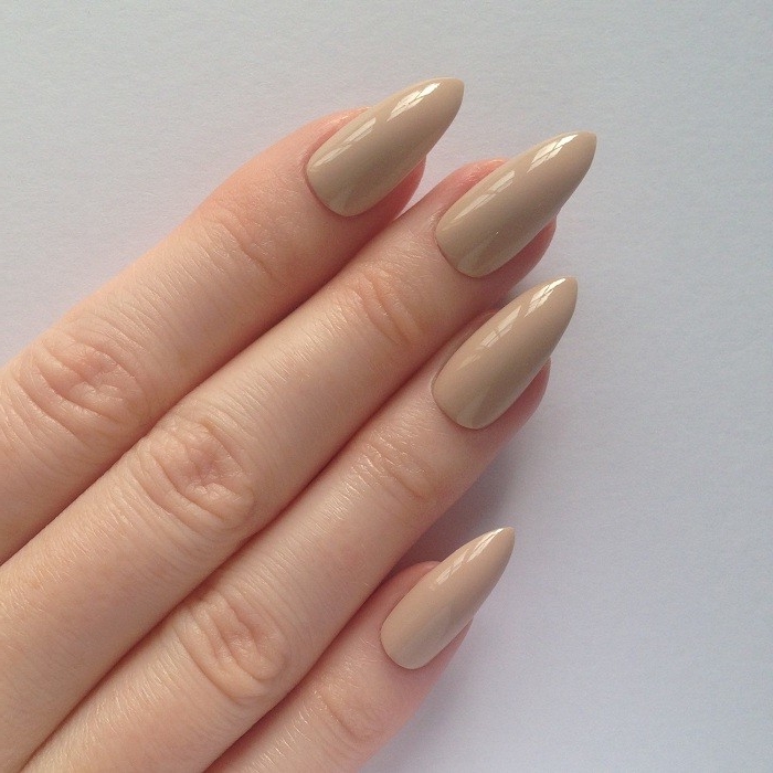 glossy and long, pointy oval nails, in a pinkish-beige color, nude nail designs, on long pale fingers