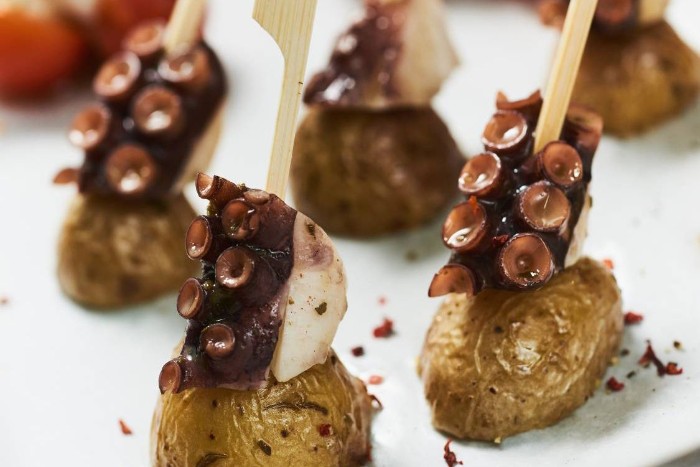 baked potatoes with skins, topped with cooked octopus pieces, appetizers for a crowd, with wooden skewers