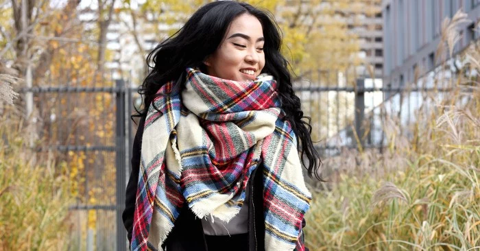 east asian woman, with black wavy hair, smiling while wearing an oversized, plaid scarf in white, and blue, red and grey, how to wear a square scarf