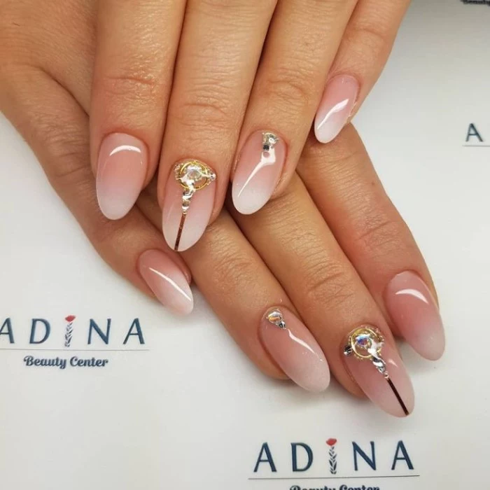 smooth and glossy oval shaped nails, decorated with gold and silver rhinestones, and featuring an ombre effect french manicure