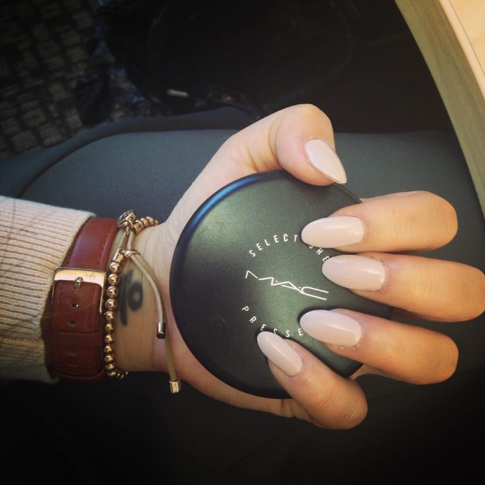 make up case in black, held by a hand with long, oval nails, painted in a milky, pale pink nail polish