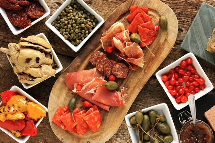 selection of easy appetizers for a crowd, wooden board with prosciutto and salami, dishes with vegetables