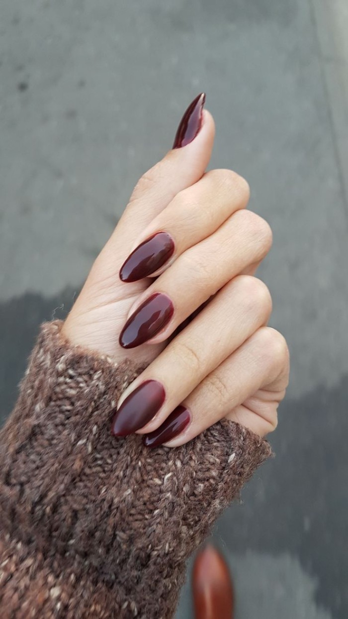 dark burgundy red nail polish, on acrylic nail shapes, worn by a pale hand, dressed in a brown, chunky knitted sleeve