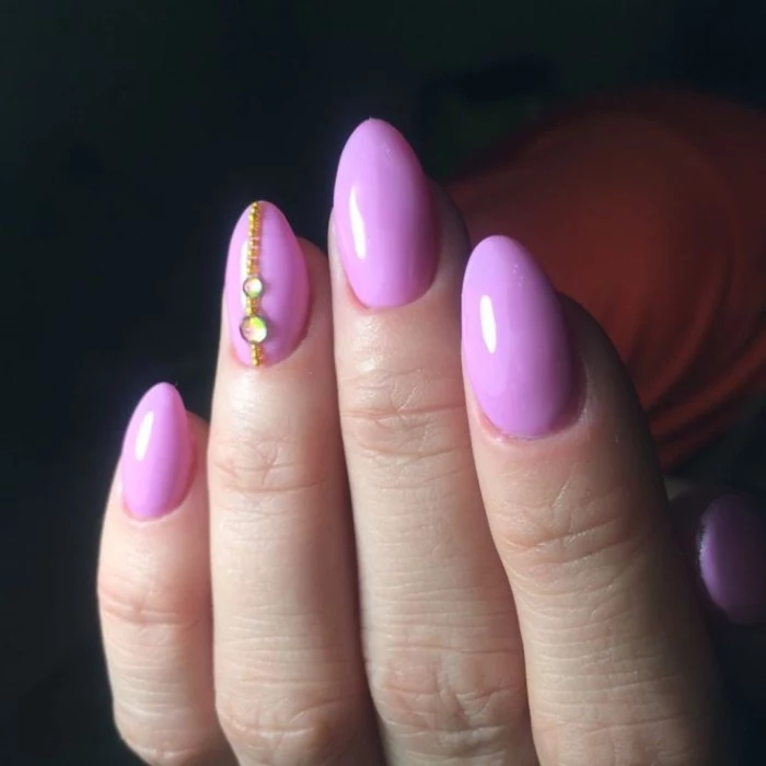 iridescent and gold rhinestones, on the ring finger nail, of a pale hand with short pointy nails, and pink manicure