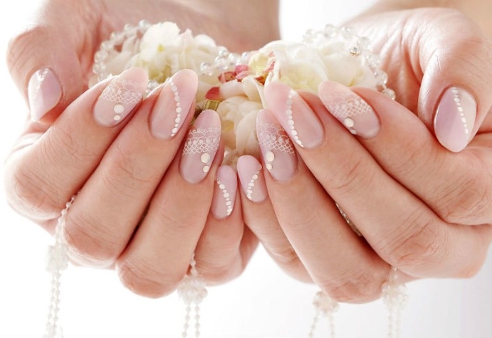 wedding manicure idea, oval nails painted in nude pink, and decorated with pearl-like, white nail decal stickers, on two hands, holding flower petals