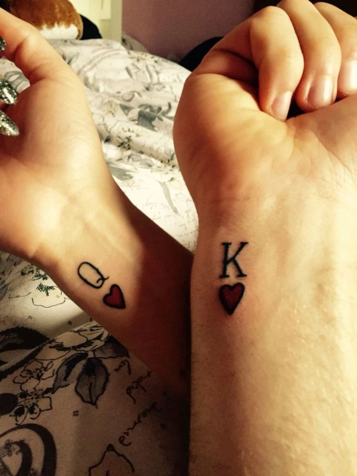 symbols for queen and king of hearts, from playing cards, tattooed on the wrists of two hands, matching tattoos for couples in love, red and black ink