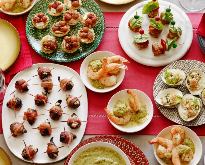 several plates filled with hor dorves, savory tartlets with vegetables, prawns and mussels, bacon-wrapped olives and more