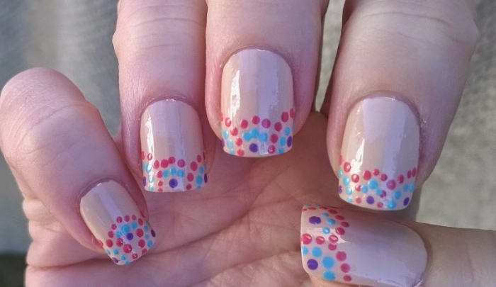 teal and navy blue, and red dots, decorating the tips of five suqare nails, painted in nude, pinkish-beige nail polish