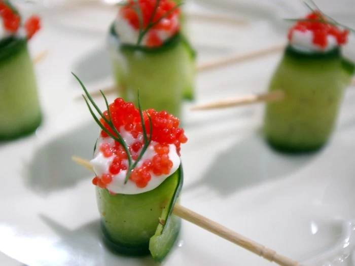 cucumber rolls stuffed with white sauce, red caviar and dill, hors dourves, skewered and placed on a white plate