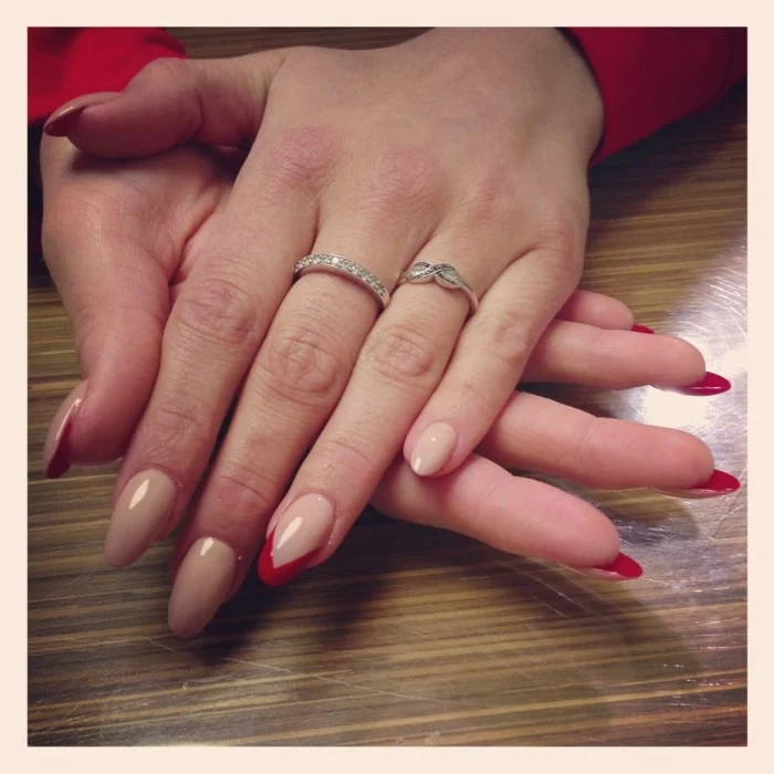 nails painted in nude beige on the outside, and red on the inside, and featuring small red details, long oval manicure, on pale slim hands