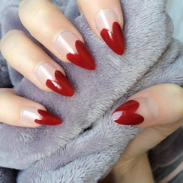 heart shapes painted in dark red, on the tips of a long, pointy manicure, with clear nude nail polish, on a hand, holding light grey fabric