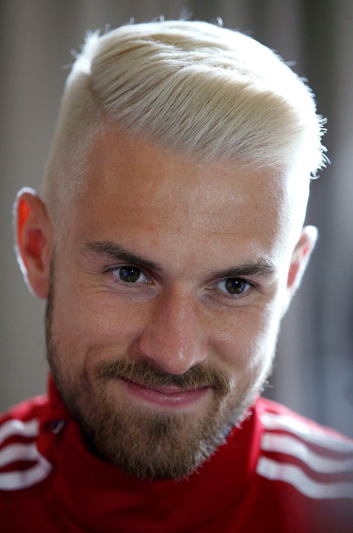 platinum blonde hair, worn by a smiling man, with short beard and mustache, short sides long top haircut, red adidas tracksuit top