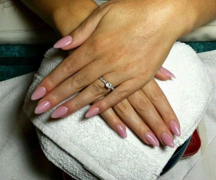 diamond ring on one of two hands, both resting on a white towel, with an almond manicure, painted in a pale pink nail polish