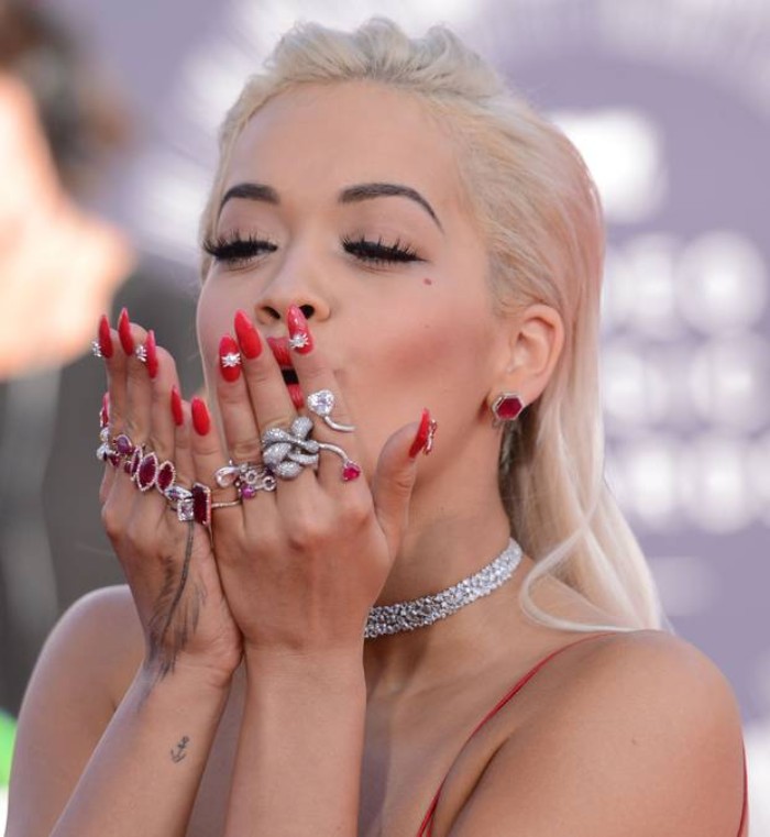 chunky silver rings, decorating the hands of rita ora, with long and sharp, bright red manicure, featuring large rhinestones