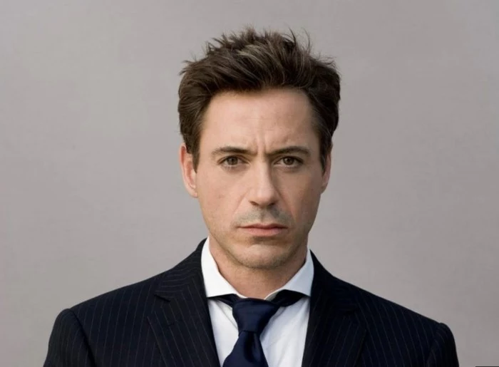 a younger robert downey jr, dressed in a pinstripe suit, with a white shirt, and a black tie, wearing a short, brunette crew cut