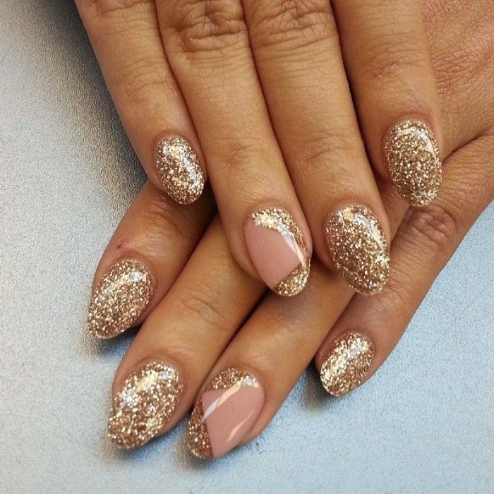 tan hands with oval manicure, featuring pink nude nails, almost entirely covered in gold glitter