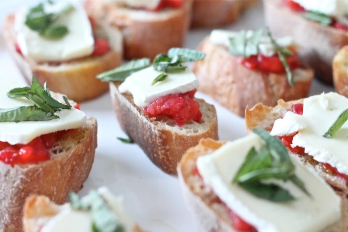 simple bruschetta with salsa, brie and fresh basil leaves, on a white surface, seen in a close up
