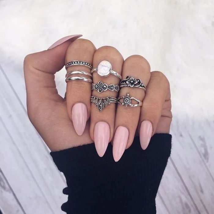 boho-style silver rings, on a hand wearing a black sleeve, and long pointy oval nails, in pale pink,