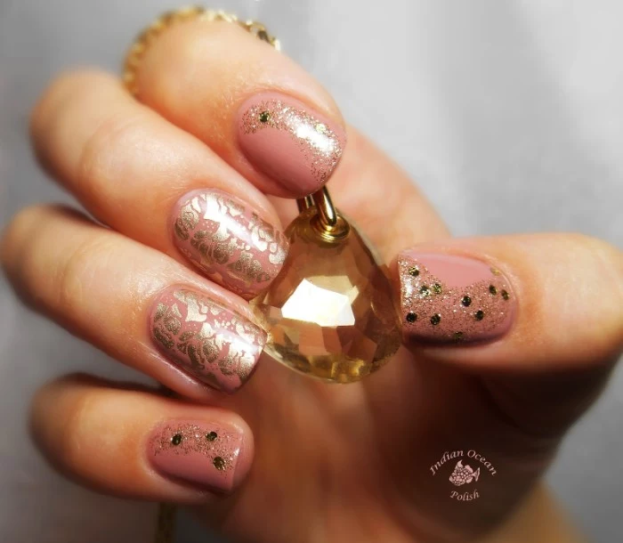 shimmering metallic motifs, fine gold glitter, and black decorative flakes, on top of a manicure, with nude nail polish, hand holding a crystal pendant