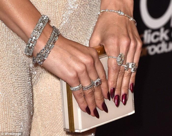 clutch bag in white and gold, held by two hands, with several rings and bracelets, pointy nails in dark shiny red