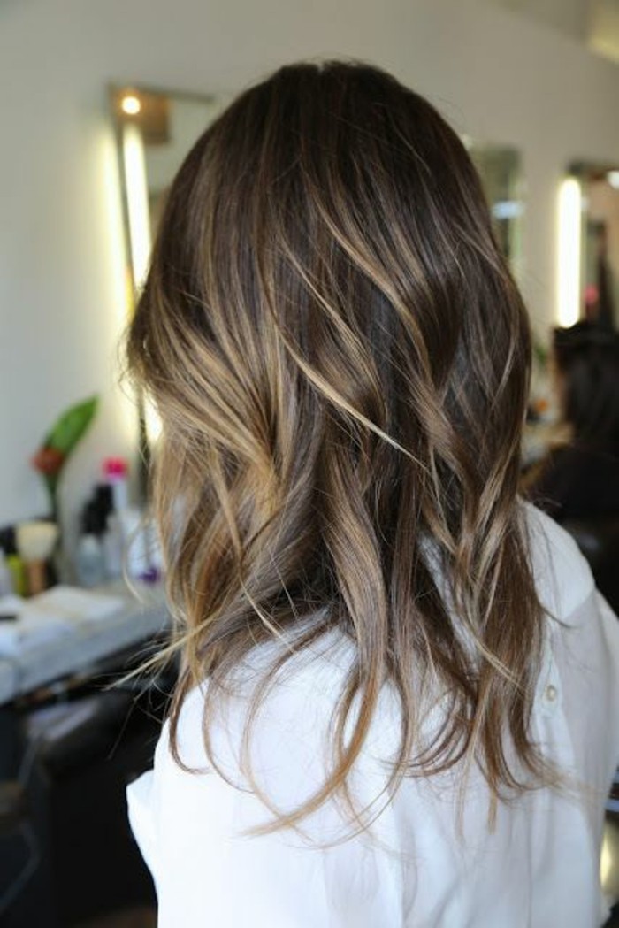 ash-blonde highlights, on wavy brunette hair, worn by a woman dressed in white, balayage dark hair, seen from the back