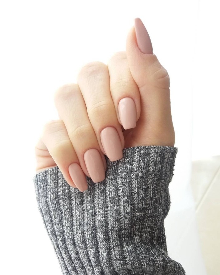 simple powder pink nude nails, with squoval shape, on a hand with folded fingers, in a long grey knitted sleeve