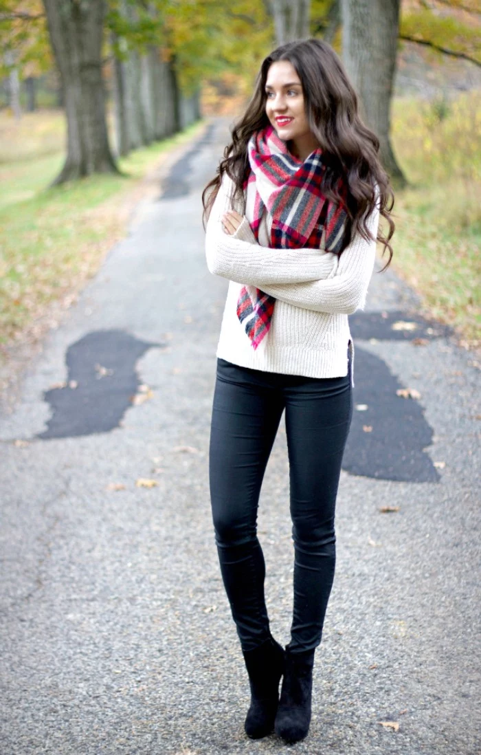 knitted sweater in white, worn with black skinny trousers, black high heeled ankle boots, and a large plaid scarf, by a smiling brunette woman