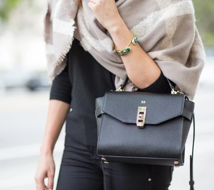 arm bag made from black leather, worn by a woman, dressed in black, with a creamy grey oversized shawl, featuring off-white patterns, draped around her shoulders, how to fold a blanket scarf, seen in close up