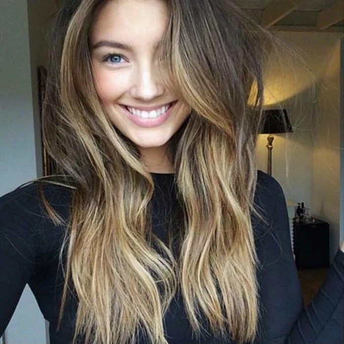 happy-looking young woman, with blonde balayage dark hair, wearing a black sweater