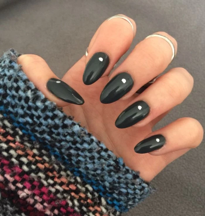 multicolored knitted sleeve, worn by a pale hand, with folded fingers, and oval shaped nails, painted in black nail polish, and decorated with white dots