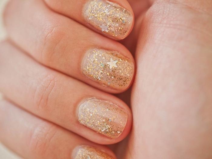 tiny stars and fine gold glitter, decorating four short nails, seen in extreme close up, nude nails with glitter