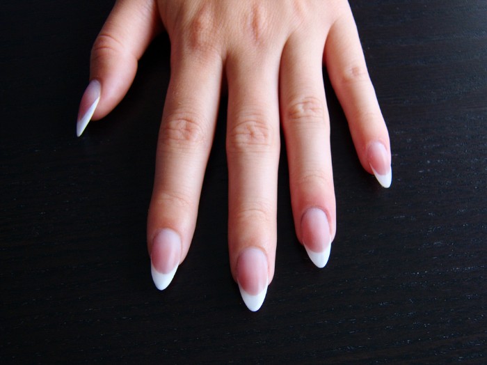 simple french manicure, on a hand with long finhers, and pointy nails, resting in a dark surface