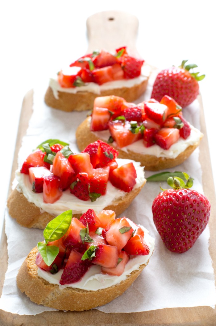 four bruschetta with ricotta, chopped strawberries and basil leaves, hor d oeuvres, placed on a wooden chopping board