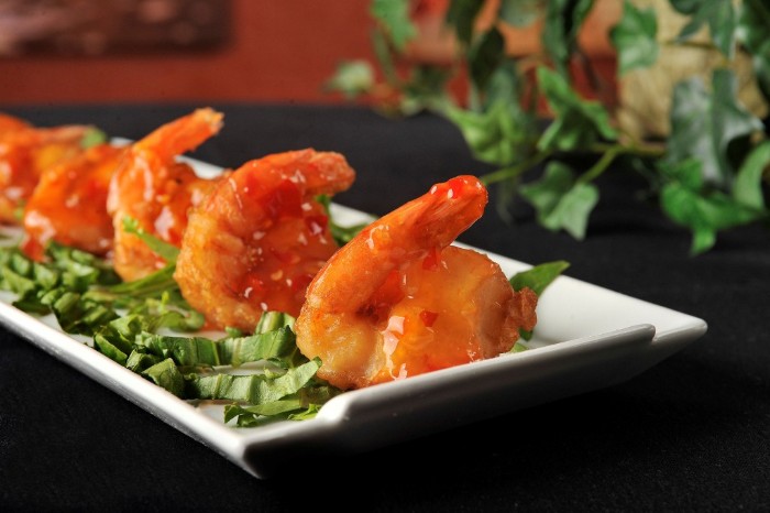 rectangular white plate, containing chopped leafy green veg, and several prawns, with sweet chili sauce, hors dourves