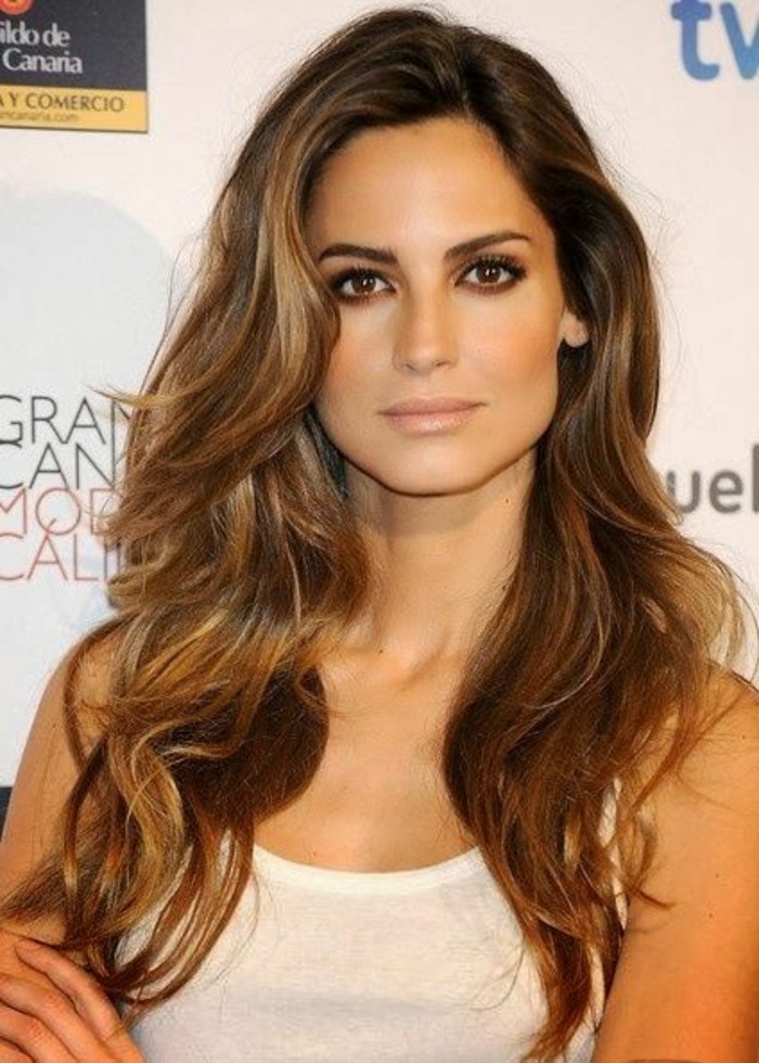 side-parted wavy brunette hair, with caramel balayage, on a young woman, with dark eyes, wearing a white tank top