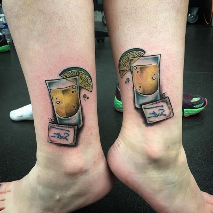 lime wedge on a tequila shot, with a small pack of salt nearby, matching friend tattoos, done in full color, on the ankles of two legs