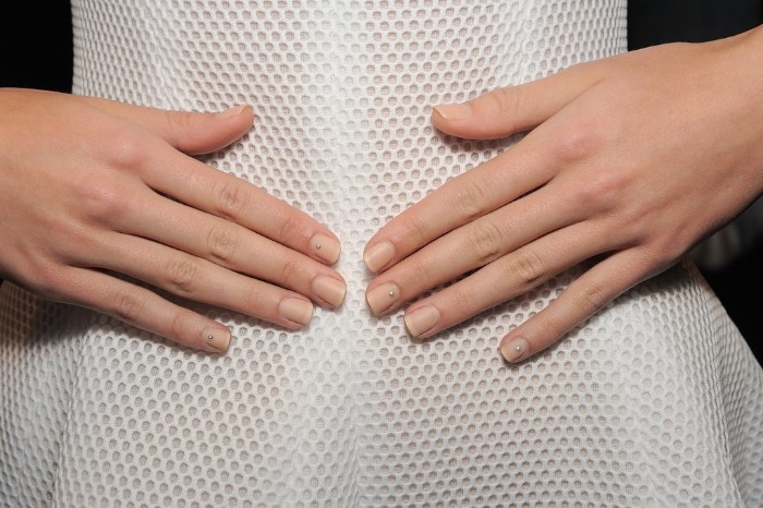 slim woman in a white dress, made from textured fabric, hands with plain, nude nail designs, placed on her stomach