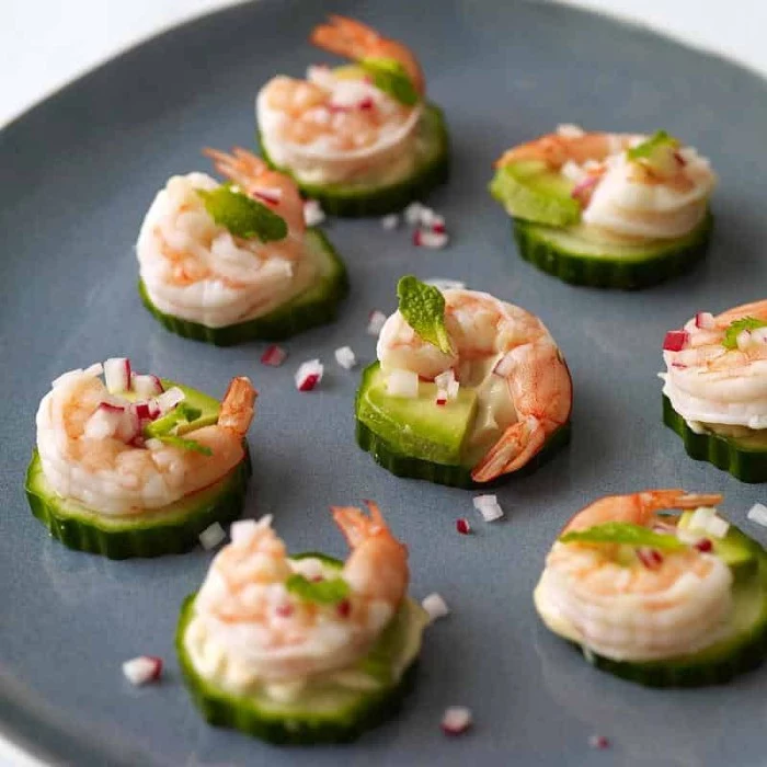 radish sprinkled on top of several appetizers, made with cucumber slices, topped with prawns