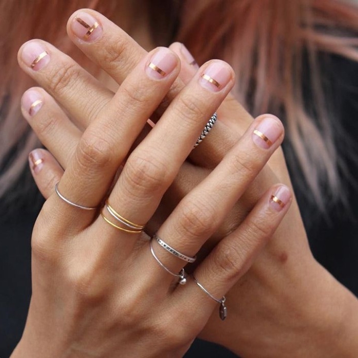 very short bare nails, each decorated with a thin, mettalic gold stripe, on two hands, with multiple thin rings