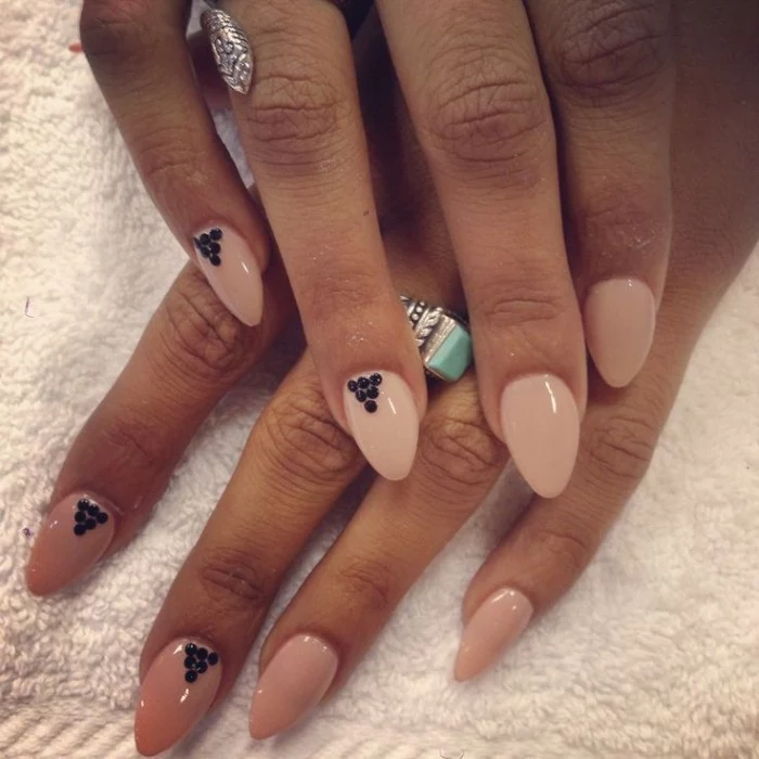 tan hands with nude nail polish, decorated with small black dots, pointy nails with almond shape