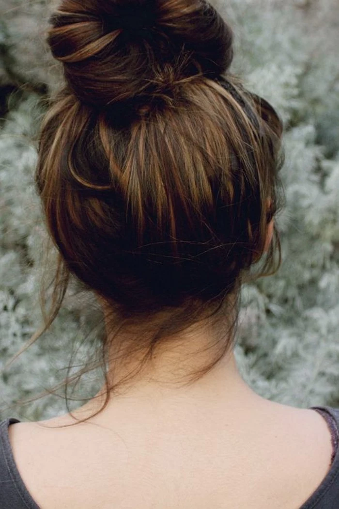 bun on top of the head of a brunette woman, with subtle dark blonde highlights, brown hair with blonde highlights, seen from the back