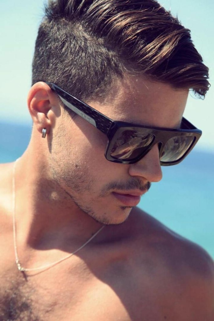 sunglasses worn by a young man, with stubble on his chin, and upper lip, short sides long top haircut, on dark brunette hair